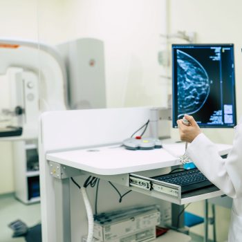 Jovem médica analisando mamografia com paciente ao fundo